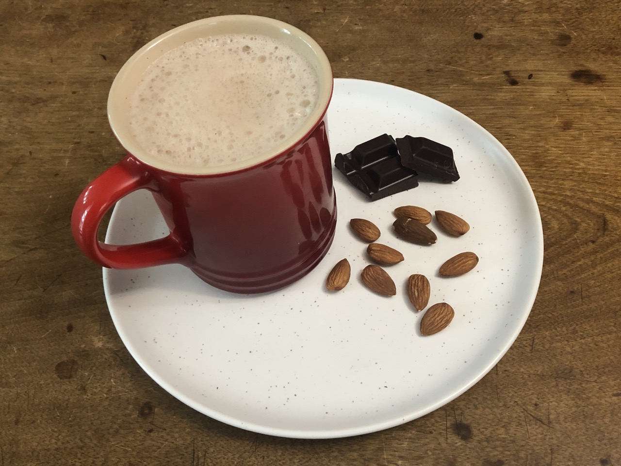 hot chocolate in a red mug on a white plate, a few squares of chocolate and almonds remain 